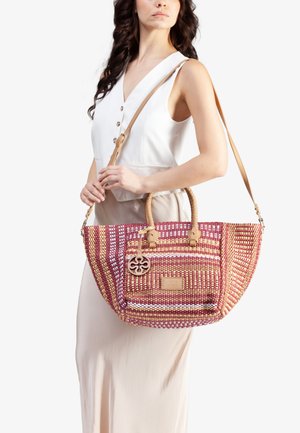 Vrouw in een witte mouwloze top en beige rok, met een grote geweven gestreepte handtas met beige leren handvatten en een schouderband.