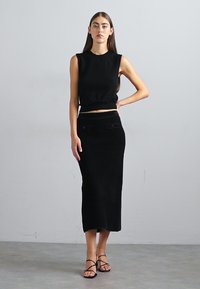 Fekete kötött crop top, kerek nyakkivágással és ujjatlan kialakítással, amely egy magas derekú fekete kötött szoknyával van párosítva, egyenes sziluettel.