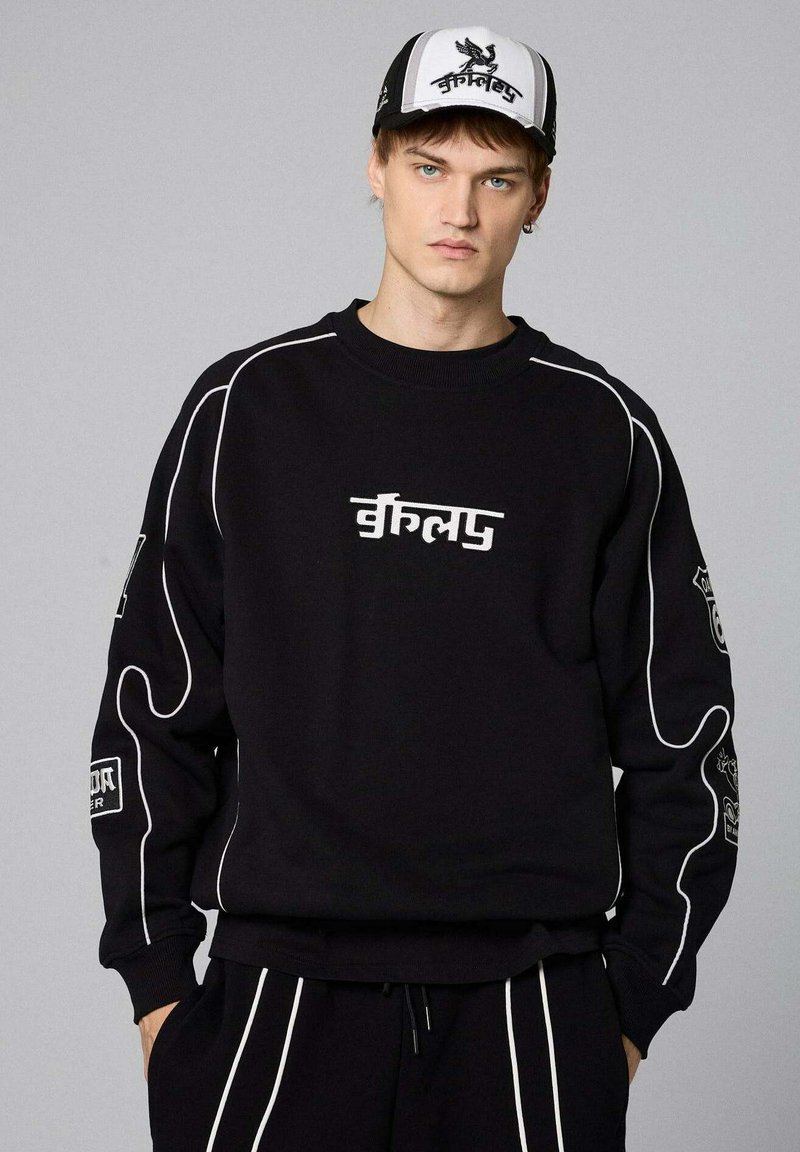 Felpa nera con accenti e loghi bianchi, caratterizzata da un collo a giro e motivi dettagliati sulle maniche. Indossata con pantaloni coordinati.