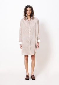 Gestreiftes Hemdkleid aus leichtem Stoff, mit vertikalen orangefarbenen und blauen Streifen, langen Ärmeln und einem weißen Kragen. Braune Schuhe runden das Outfit ab.