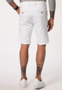 Vita denimshorts med rak passform, två bakfickor och en slät yta. Bärs med vita sneakers och dekorativa tatueringar synliga.