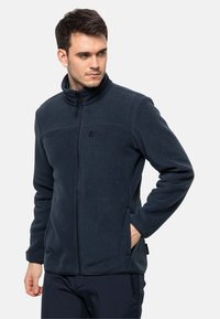 Navyblauwe fleecejack met een hoge kraag, volledige rits, twee zijzakken en een subtiele logo op de borst. Zachte textuur met een strak fit.