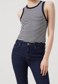 Black and white striped tank top with ribbed texture, paired with dark denim jeans featuring contrasting stitching and button closure.