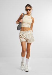 Karamelli triibuline lühike top ja sellele sobivad lühikesed püksid, kombineeritud valgete jooksu- ja sokkidega. Mudel kannab halli kotti ja kannab musti päikeseprille.