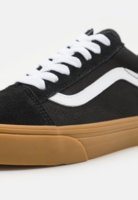 Svart mocka och kanvas sneakers med vita snören och vit sidostrand, med en gummisula och texturerat mönster på sulan.