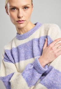 Knitted pullover in cream and light purple stripes, featuring a round neck, loose fit, and textured fabric with a soft finish.