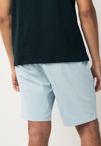 Vaaleansiniset shortsit, jotka on valmistettu sileästä kankaasta. Malli on rento, ja niissä on sivutaskut. Helmassa on siisti, suora reunus.