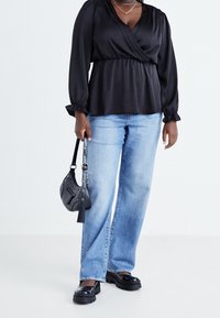 Blouse noire à manches longues, associée à un jean bleu clair à jambes larges. Un petit sac à main noir et des chaussures noires chunky complètent la tenue.