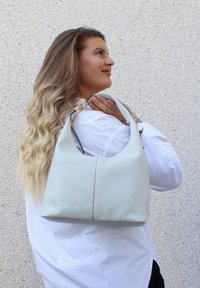 Hobo-väska i mjukt, ljusblått läder med en rundad form, med guldaccessoarer och en kontrastsöm längs mittsömmarna.