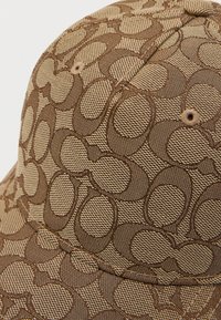 Καφέ καπέλο κατασκευασμένο από ύφασμα, με υφασμένο σχέδιο από διασυνδεόμενους κύκλους, με ραμμένη κορυφή και αεραγωγούς. Ανθεκτικός σχεδιασμός για καθημερινή χρήση.