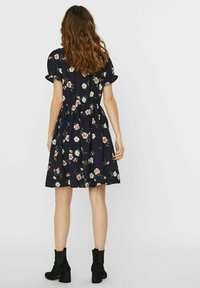 Blumenkleid aus marineblauem Stoff mit kurzen Puffärmeln, tailliertem Bund und ausgestelltem Rock. Mit rosa und weißen Blumen durchgehend bedruckt. Schwarze Stiefeletten.