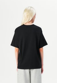 Black cotton t-shirt with a relaxed fit, short sleeves, and a crew neck, shown from the back against a plain white background.