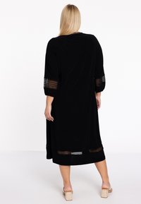 Schwarz langes Kleid mit relaxed Fit, das strukturierte Akzente an den Ärmeln und am Saum aufweist. Hergestellt aus glattem Stoff, mit Dreiviertelärmeln.