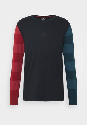 Camiseta negra de manga larga con anchas rayas horizontales rojas en la manga izquierda y rayas azules en la manga derecha, cuello redondo y un logo sutil en la parte delantera.
