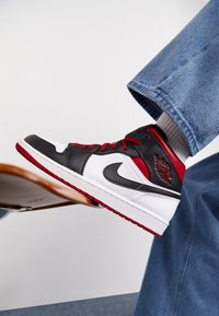 Vysoké tenisky v černé, bílé a červené barvě; kožený materiál; výrazný znak Nike Swoosh; strukturovaný povrch; červené tkaničky.
