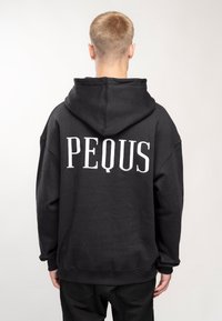 Felpa nera oversize con cappuccio, caratterizzata da una tasca a canguro frontale e una grande stampa bianca "PEQUS" sul retro. Realizzata in tessuto morbido.