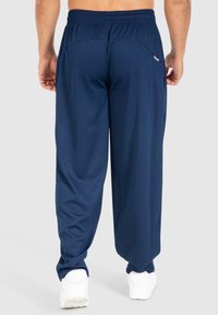 Marineblauwe sportbroek met een gestructureerd ribbelontwerp, elastische tailleband en twee achterzakken, gecombineerd met witte sneakers.