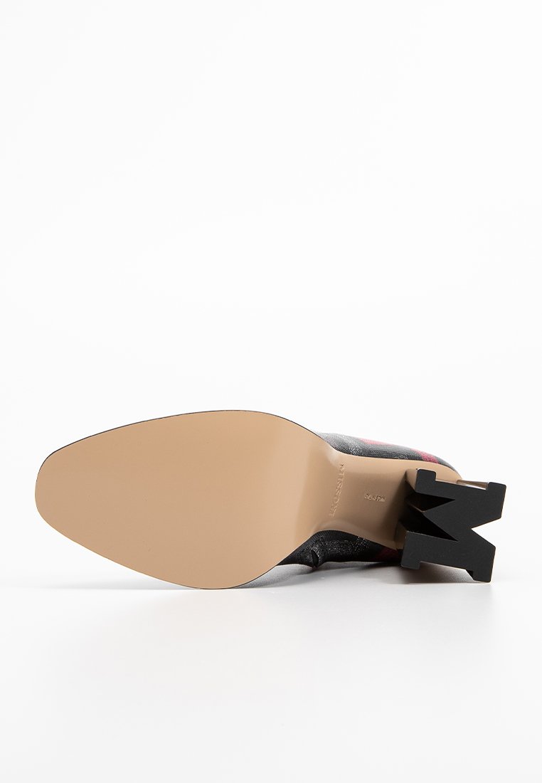 Schwarzer Absatzschuh mit einem markanten geometrischen Absatzdesign und einer glatten, tanfarbenen Sohle. Das Obermaterial besteht aus strukturiertem Material mit roten Akzenten.