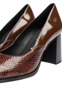 Scarpe col tacco alto in vernice marrone con texture in pelle di serpente. Design con punta quadrata e tacco a blocco. Fodera interna nera.