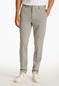 Pantalones ajustados de color gris claro con una textura suave, que presentan un botón delantero, bolsillos laterales y piernas ceñidas, combinados con zapatillas blancas.