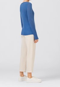 Blaues, eng anliegendes Sweatshirt mit langen Ärmeln, rundem Ausschnitt und weicher Textur. Kombiniert mit hellbeigen, gekürzten Hosen und weißen Turnschuhen.