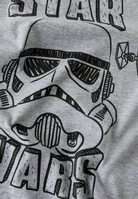 Hall hall T-särk, millel on must graafika tormi sõduri kiivrist ja julge "STAR WARS" tekstiga. Sile puuvillane tekstuur. Lihtne, ühevärviline disain.