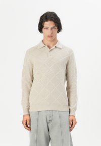 Suéter de punto beige claro con un patrón de diamantes, mangas largas y cuello tipo polo. Presenta una textura tejida y puños y dobladillo acanalados.