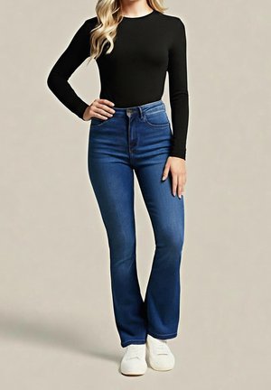 Femme portant un haut noir à manches longues, un jean bleu taille haute et des baskets blanches, debout avec une main sur la hanche devant un fond uni.