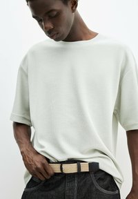 Lys grøn, ribbet t-shirt med korte ærmer, båret med et sort og vævet beige bælte, parret med mørk denim jeans. Tekstureret stof og afslappet pasform.