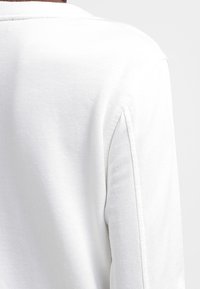 Vit sweatshirt med en strukturerad tygkvalitet, ribbad rund hals och axelsömmar. Utstrålar mjuka, rena linjer och en avslappnad passform.