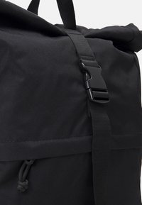 Mochila negra tipo roll-top hecha de tejido duradero, con correas ajustables, cierre de hebilla lateral y un acabado texturizado.