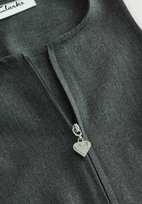 Mörkgrå zip-up-plagg med rund halsringning och en silverhjärtformad dragkedjehake, tillverkat av ett texturerat tyg.