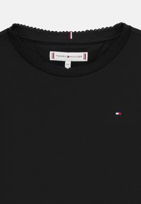 Czarna koszulka z krótkim rękawem i okrągłym dekoltem, z teksturowanym wykończeniem oraz małym logo w kolorach czerwonym, białym i niebieskim na klatce piersiowej.