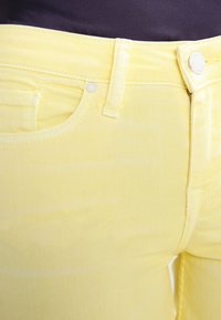 Jean en denim jaune avec une surface texturée, dotés de poches avant, d'une fermeture à bouton et de coutures contrastantes le long des coutures.