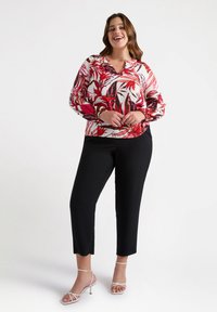 Blusa floreale con motivi di foglie rosse e nere, scollo a V e maniche lunghe, abbinata a pantaloni neri a sigaretta e tacchi bianchi con cinturini.