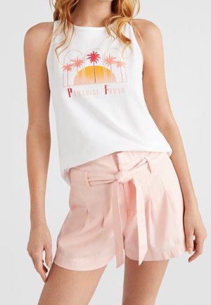 Kobieta ubrana w biały top na ramiączkach z czerwonymi palmami i napisem „Paradise Found”, w połączeniu z różowymi, wysokim stanem szortami wiązanymi w talii.