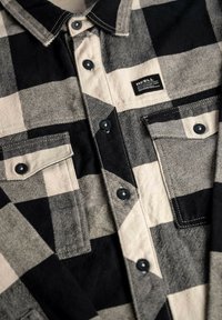 Black and white plaid shirt made of textured fabric featuring a button-up front, two chest pockets, and a small brand label.
