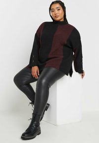 Överdimensionerad svart och vinröd stickad tröja med sidsprund och metallknappdetaljer, matchad med glänsande svarta läderleggings och snörstövlar.