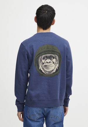 Felpa blu navy in un tessuto morbido, con una grafica del volto di un gorilla all'interno di un casco sul retro. Vestibilità casual con polsini a costina.