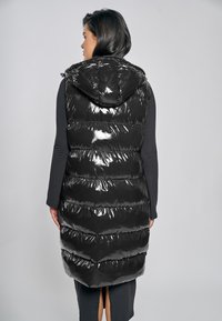 Schwarze, glänzende Steppweste mit Kapuze, die horizontale Steppabschnitte, eine lange Passform und einen Seitenschlitz für Bewegungsfreiheit aufweist.