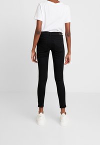 Jeans skinny negros con una cintura de medio tiro, que presentan una textura de denim suave, bolsillos traseros y combinados con zapatillas blancas.