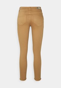 Pantalon ajusté couleur sable vu de dos avec deux poches arrière, passants pour ceinture et ourlets effilochés sur un fond uni.