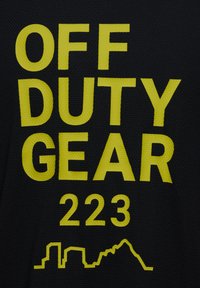 Zwarte stof met vet gele tekst "OFF DUTY GEAR 223" boven een grafische silhouet van een stadsbeeld.