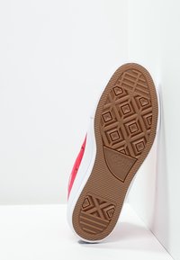 Sneaker rossa in tela con suola in gomma bianca, caratterizzata da una suola esterna marrone testurizzata con motivo a diamante e un marchio ben visibile sul tallone.