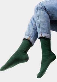 Zielone skarpetki w prążki z miękkiego materiału, założone do podwiniętych jasnoniebieskich dżinsów, ukazujące teksturę i kontrast kolorystyczny.
