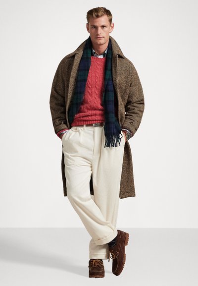 Abrigo de pata de gallo marrón, suéter de punto de cable rojo, camisa a cuadros azul, pantalones de pana color crema, zapatos mocasines marrones, bufanda azul marino con flecos.