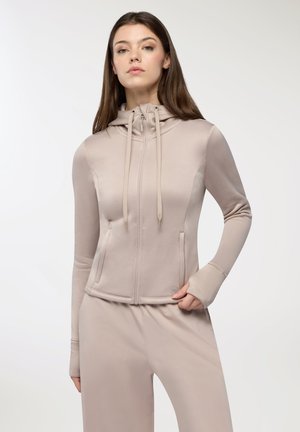 Felpa con zip di colore beige chiaro, dal design aderente, con tasche a marsupio e lacci sul cappuccio. Tessuto morbido e liscio; maniche lunghe con fori per i pollici.