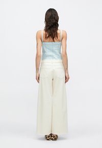 Top sin mangas de color azul claro con un diseño ajustado, combinado con pantalones anchos blancos. Se ven zapatos con estampado de leopardo en la parte inferior.