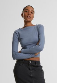 Ljusblå, långärmad topp med båtformad halsringning, mjuk textur och figurnära design, i kombination med en högmidjad svart denimkjol.