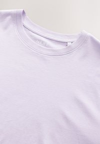 Vaaleanlaventelinvärinen T-paita, jossa pyöreä pääntie ja pehmeästä puuvillakankaasta valmistettu. Yksinkertainen ommel kauluksessa, sisäpuolella "NEXT"-merkintä.